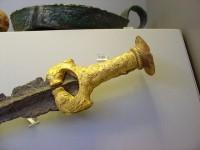 8710. Long bronze sword with ornate gold hilt revetment, decorated with spirals and ending in lion-heads. Grave Delta